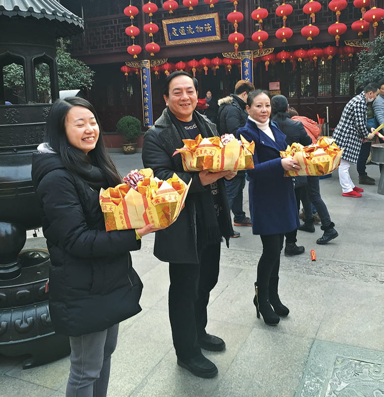Three people holding boxes of offerings in a Daoist temple