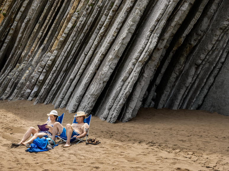 Photo of a couple relaxing at the beach with geological formations behind them