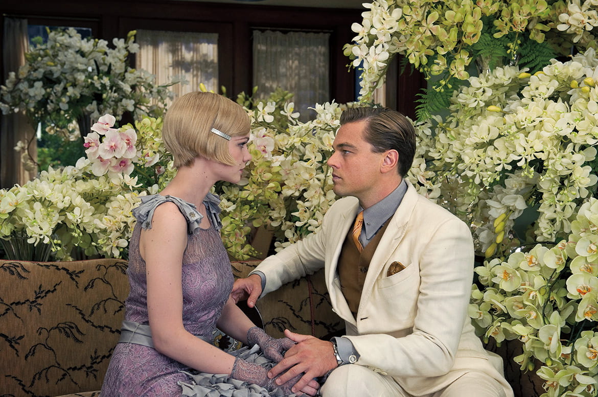Film still from Gatsby with a 1920s male and female couple seated on a garden bench, gazing at each other