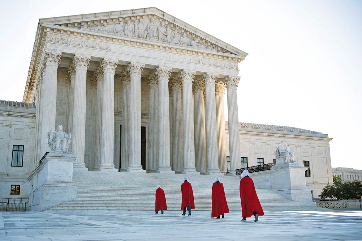 Photo of four women wearing red robes walking to the steps of the US Supreme Court building