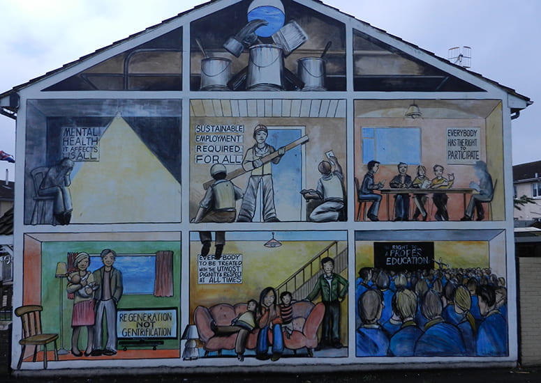 Mural on the side of a building, with household scenes labeled: Mental Health it affects us all; sustainable employment required for all; everybody has the right to participate; regenerations not gentrification; everybody to be treated with the utmost dignity & respect at all times; right to a proper education
