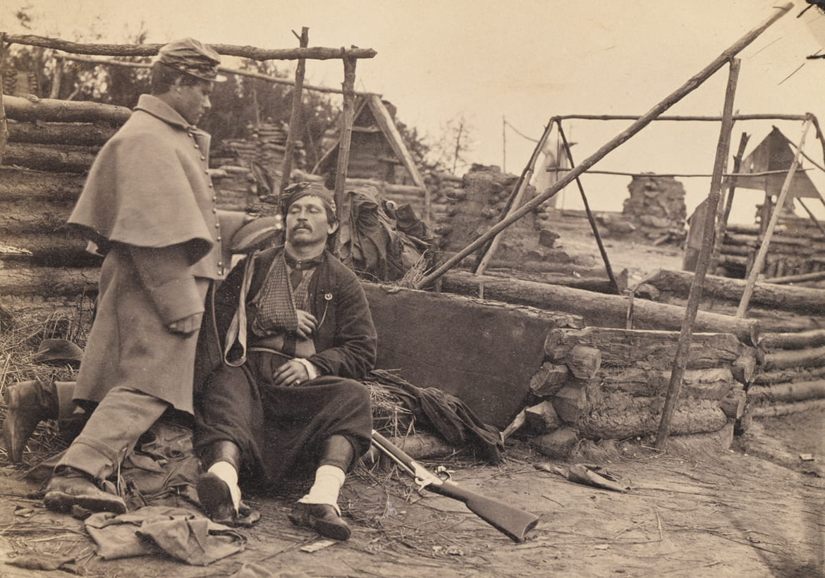 Historic photo of civil two war soldiers, one sitting on the ground with his arm in a sling