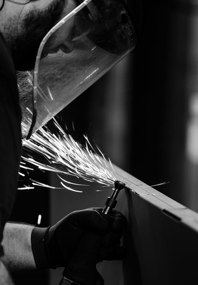 Black and white photo of a factory worker grinding metal with sparks flying