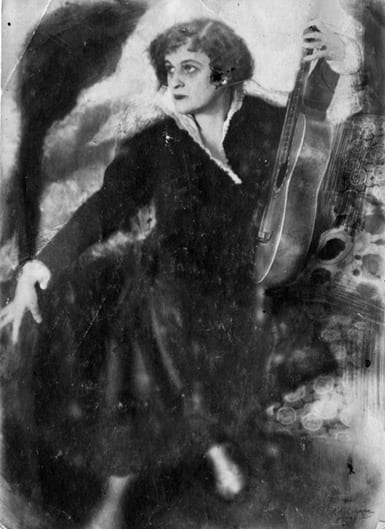 Photo of Teffi, seated, holding a guitar at her side