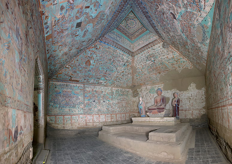 Interior view of cave 85 with painted walls and ceiling and a statue on a raised dias