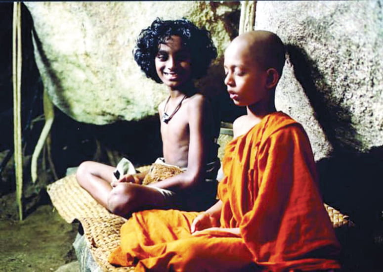Film still of a young monk meditating next to his smiling friend from Suriya Arana