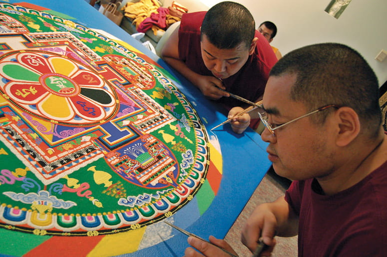 Two Buddhist monks filling in the edges of a sand mandala