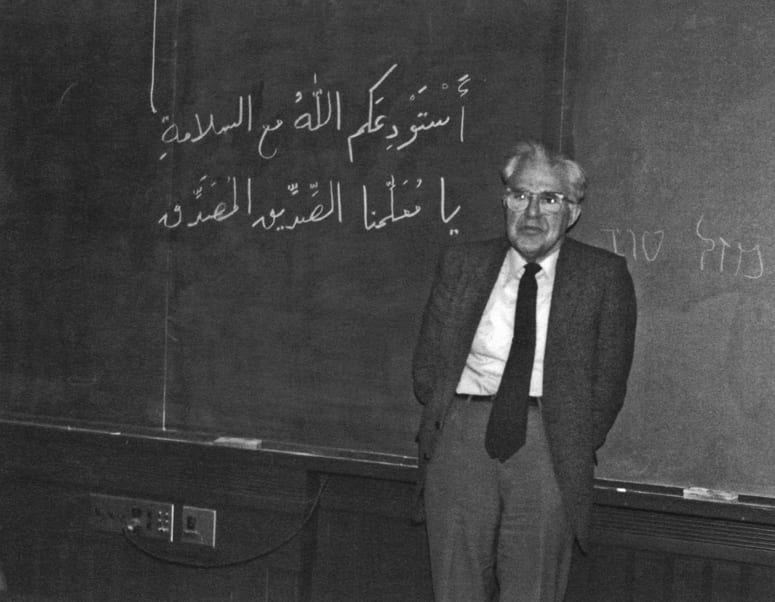 Wilfred Cantwell Smith standing in front of a chalkboard with Arabic writing on it