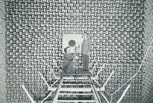 Photo of two men testing speakers inside a room covered with soundproof panels