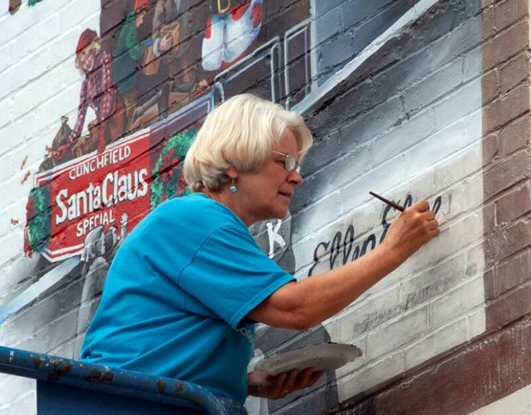 A woman painting her name onto a building mural