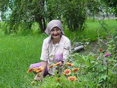 Elderly woman sitting outside in the grass by a flower garden