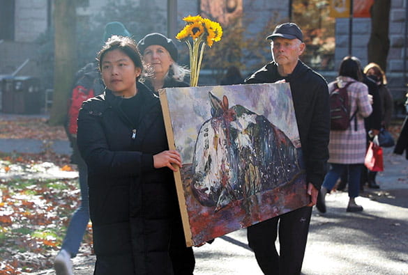 Photo of a three people carrying a large painting through the Harvard campus