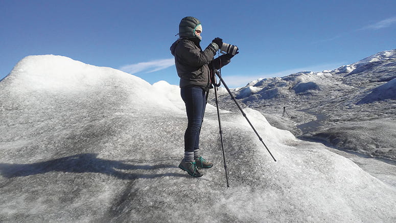 Photo of a woman with a camera on a tripod set up on top of snow and ice